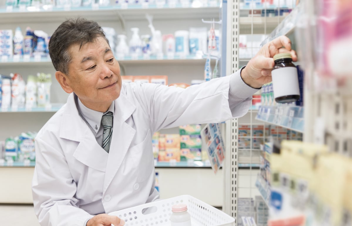 약사가 약국 선반 앞에서 약품 상자를 확인하는 장면은 어떤 뜻인가요? 관련 이미지 - 약사가 약국 진열대에서 약품을 정리하고 있습니다. 전문적인 환경에서 약품 관리의 중요성을 나타냅니다.