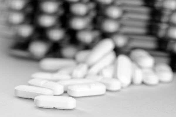 2. 알약 배치 및 고정 관련 이미지 - 하얀색 알약들이 바닥에 흩어져 있고, 배경에는 블리스터 팩으로 보이는 약품 포장이 흐릿하게 보인다. 의약품 관련 자료에 활용하기 좋다.