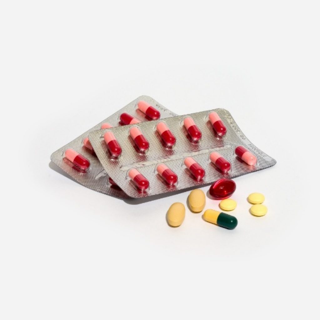 왜 이런 장면이 자주 보일까 관련 이미지 - 두 개의 블리스터 팩에 담긴 붉은색과 분홍색 캡슐, 그리고 여러 가지 색상과 형태의 알약들이 함께 놓여 있습니다. 건강 관리 및 의약품 관련 콘텐츠에 활용하기 좋습니다.